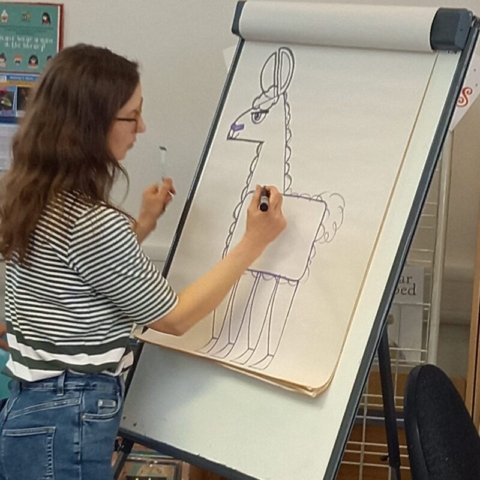 Emily Fellah demonstrating how to draw a llama on a flip chart