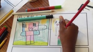 A child's hand drawing colourful robot and human characters on a comic template.