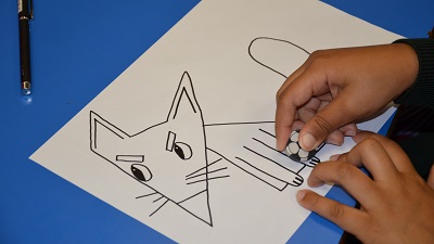 Child's hands erasing the pencil lines from a grumpy fox character they created which is drawn in black pen